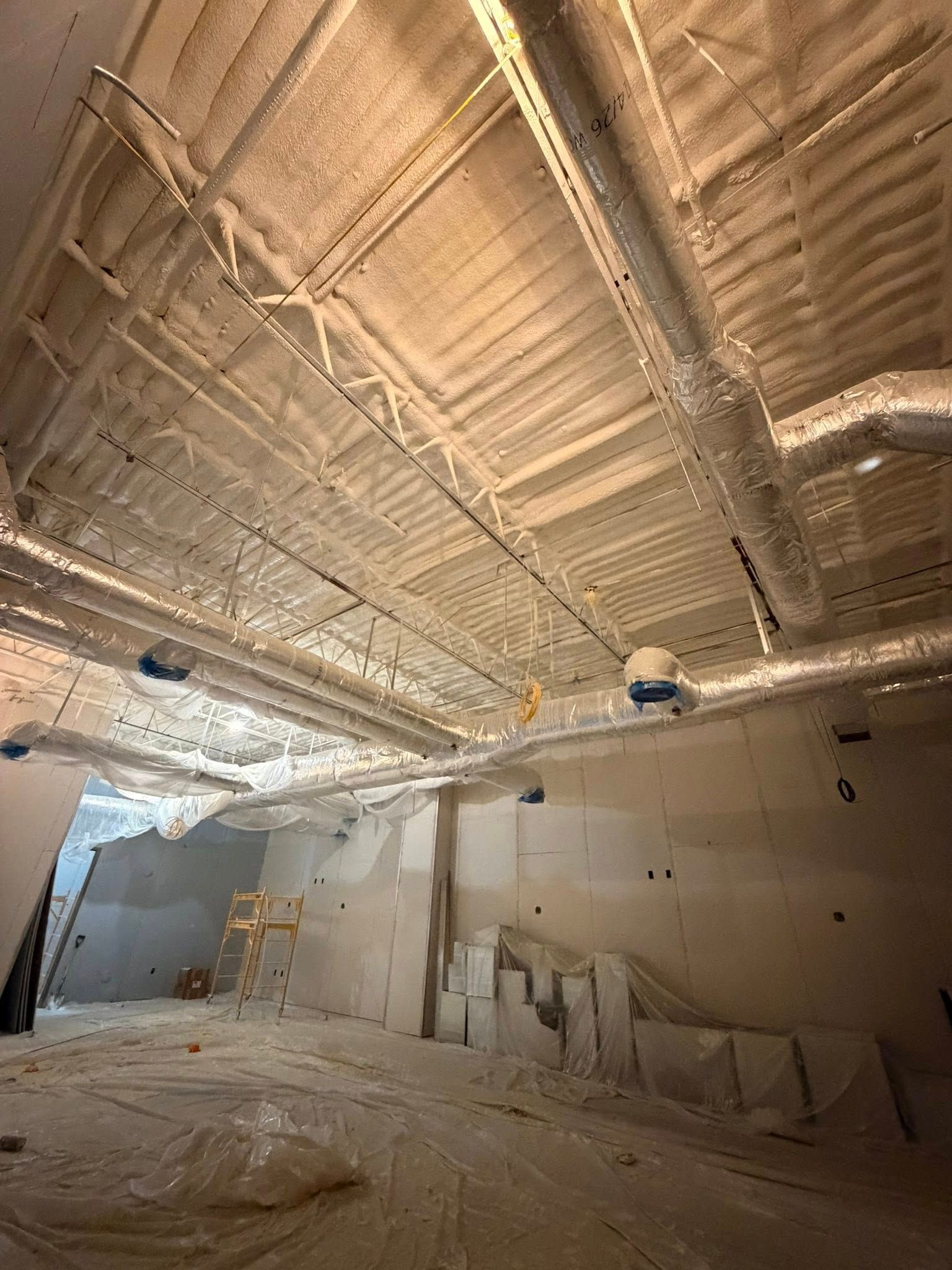 Empty construction room with exposed insulated ceiling, white walls, and scattered materials on the floor.