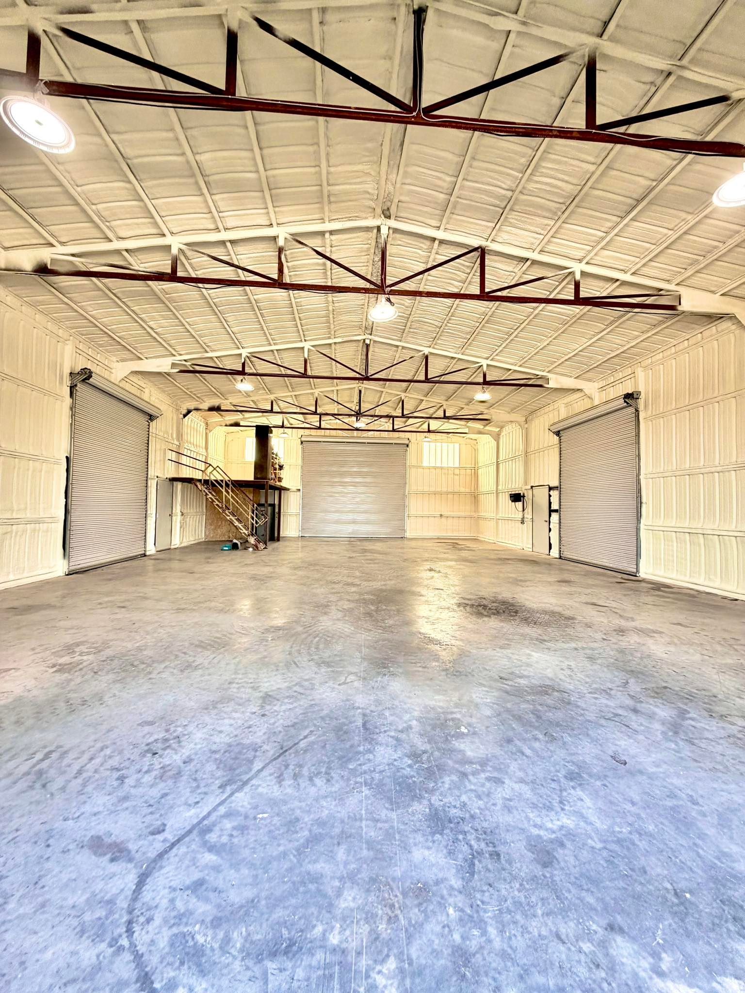 Empty industrial warehouse interior with white walls, exposed beams, and concrete floor