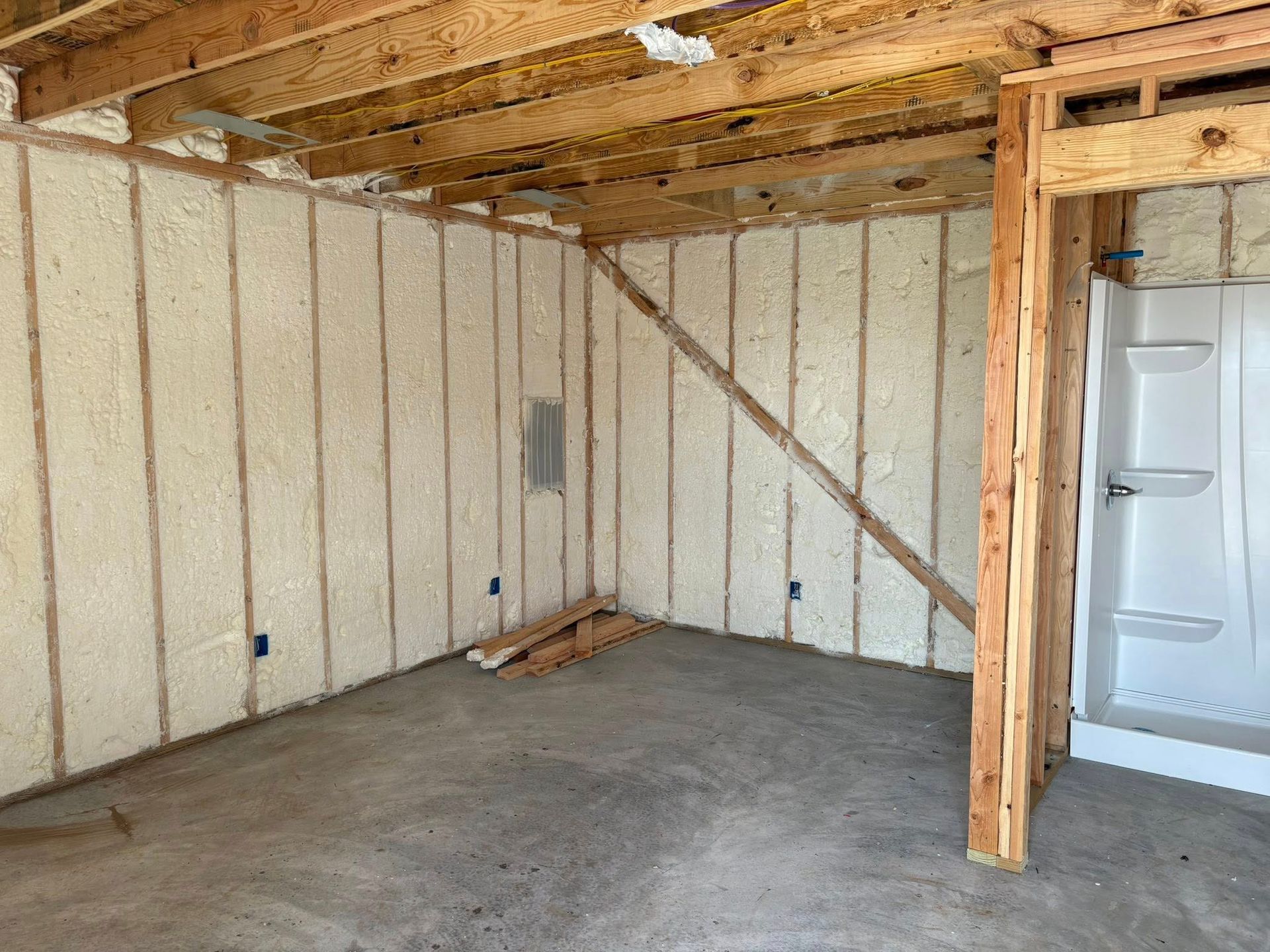 Unfinished garage interior with exposed wood beams, insulated walls, concrete floor, and a white door.
