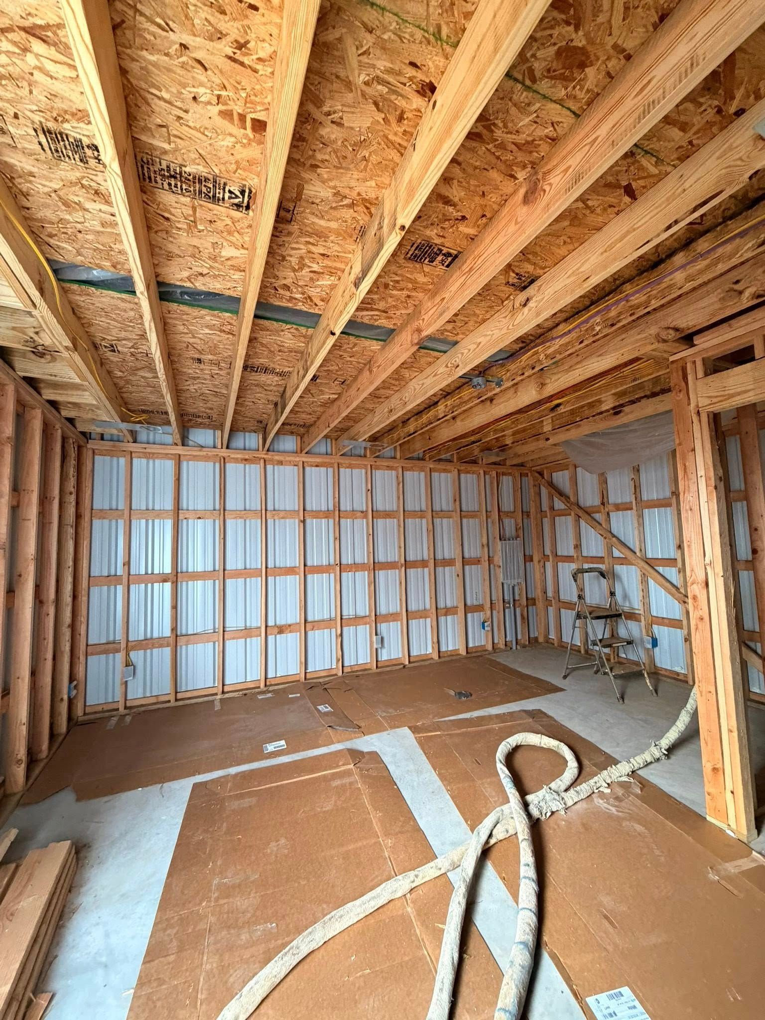 Unfinished room under construction with exposed wood framing, insulated walls, and a hose on the floor.