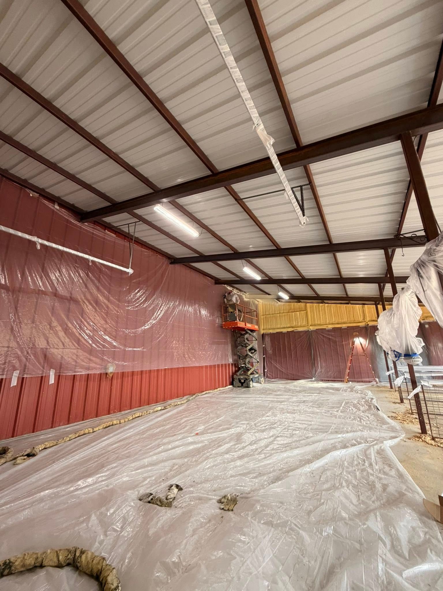 Large indoor warehouse with plastic-covered floor, red wall tarp, and exposed metal roof beams.