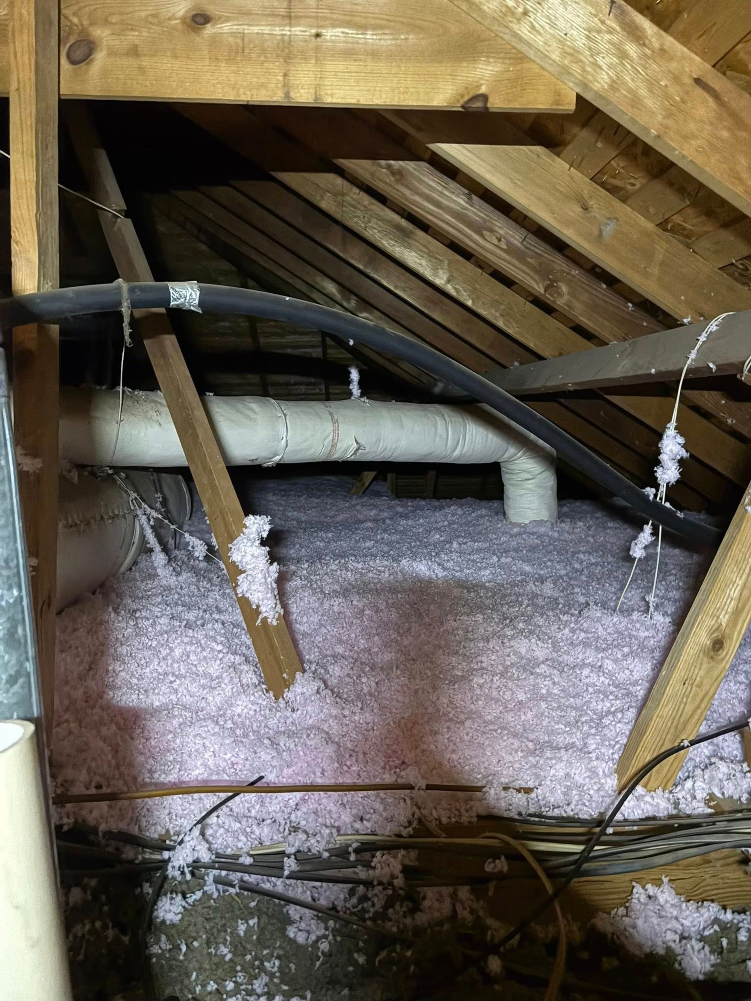 Attic with exposed wooden rafters, insulation on the floor, and white HVAC ducts running across the space