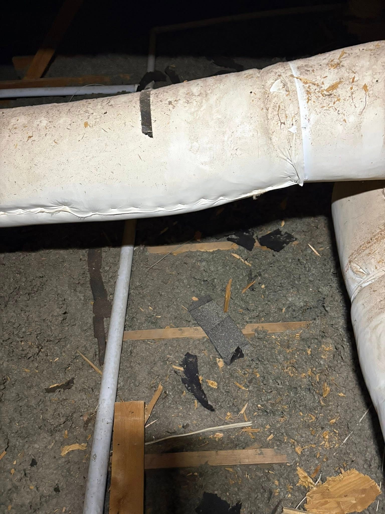 White insulated pipe crossing a dusty attic floor with debris and wood framing underneath