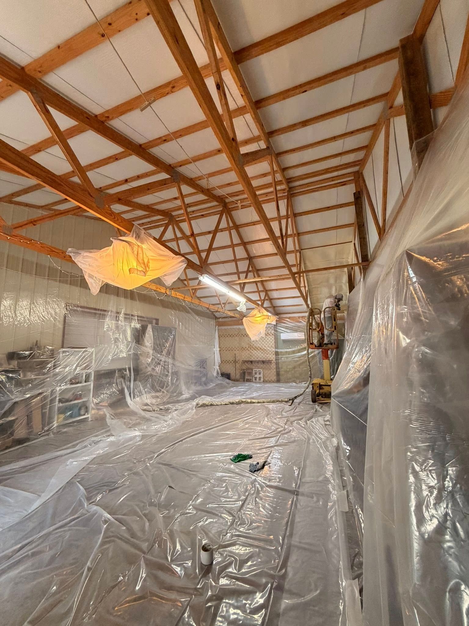 Plastic-covered interior under construction with exposed wooden roof beams and hanging lights