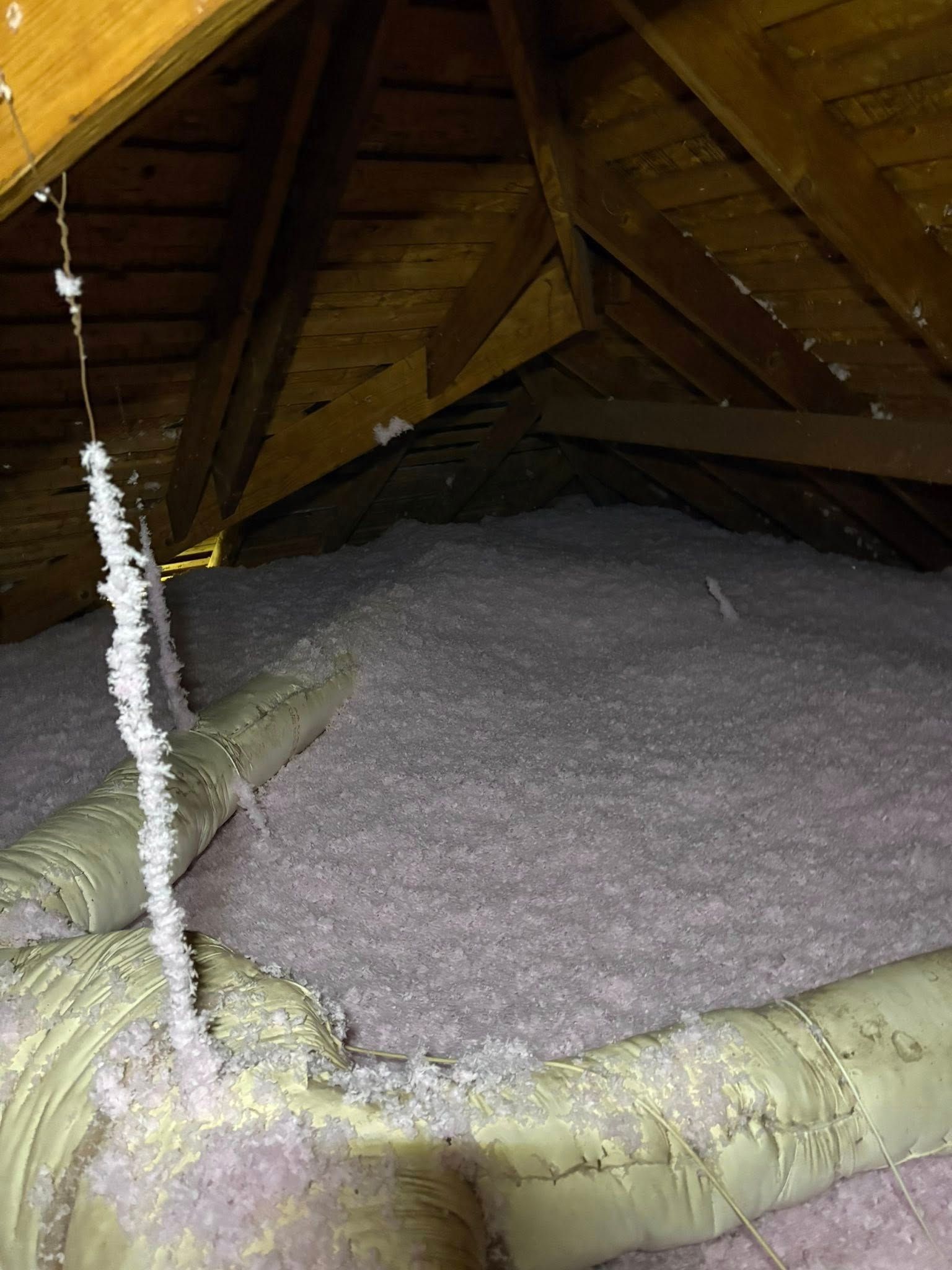 Attic with a large insulated vent pipe and a mound of gray granular material on the floor