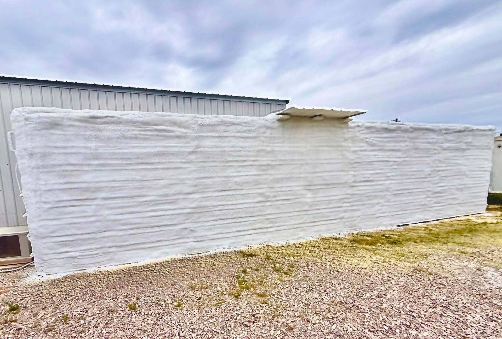 Large white wrapped wall or structure beside a metal building on gravel ground