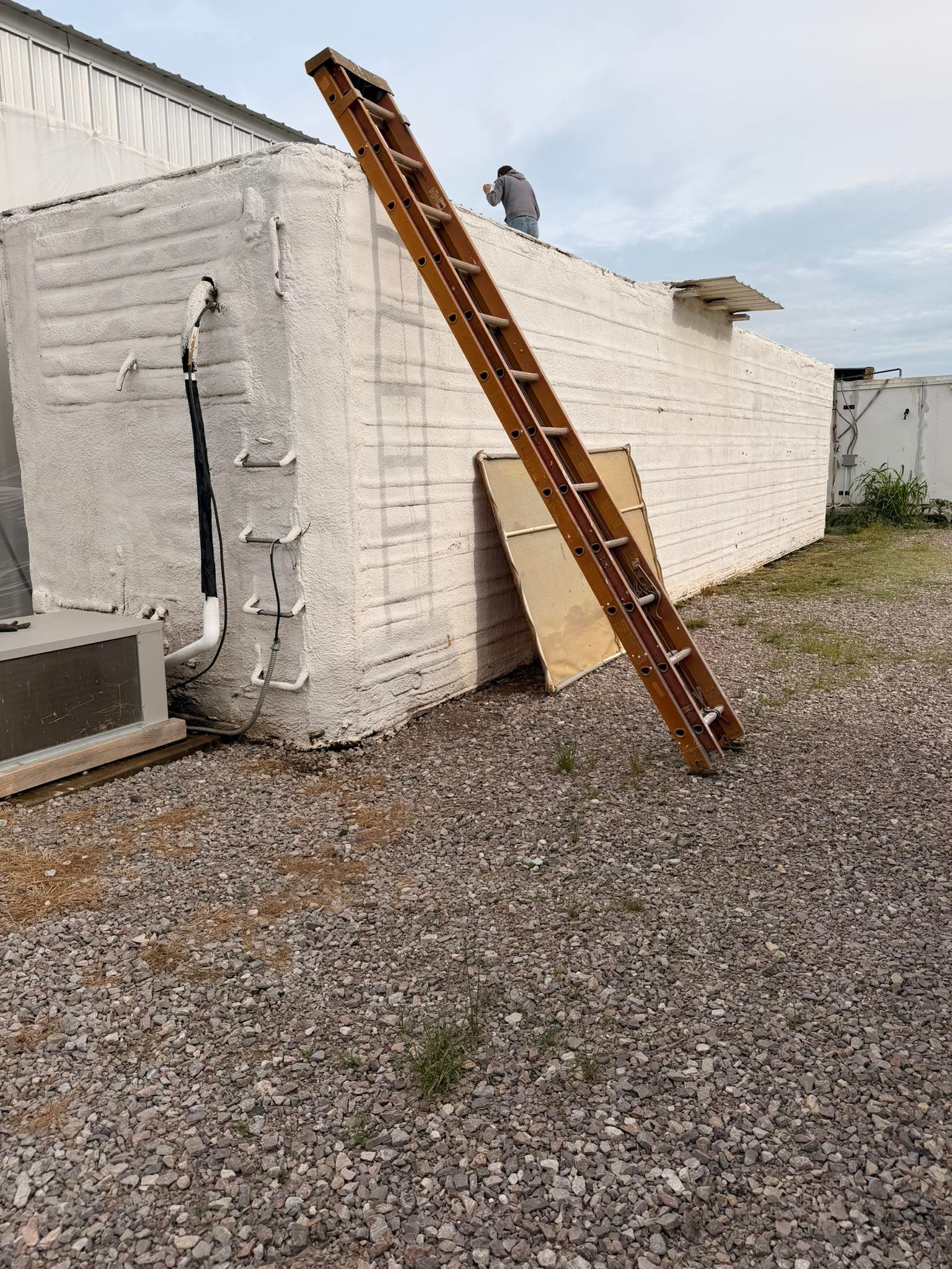 Wooden ladder leaning against a white building wall beside a gravel yard