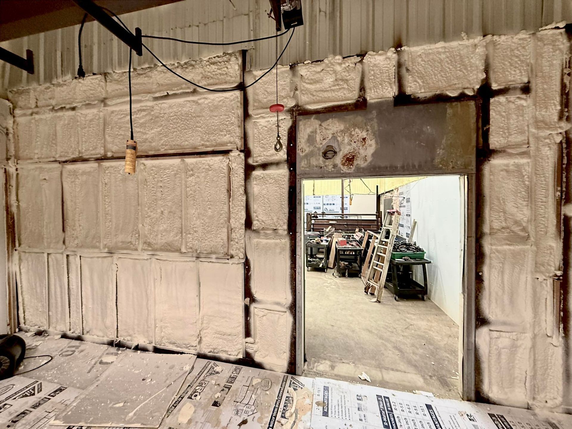 Industrial warehouse interior with insulated wall panels and an open doorway to a cluttered work area