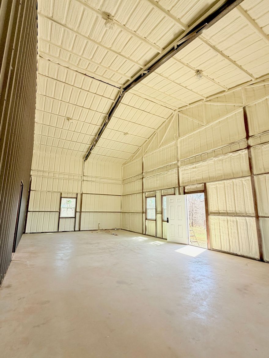 Large, dim warehouse interior with muddy floor, exposed ceiling, and bright work lights in the distance