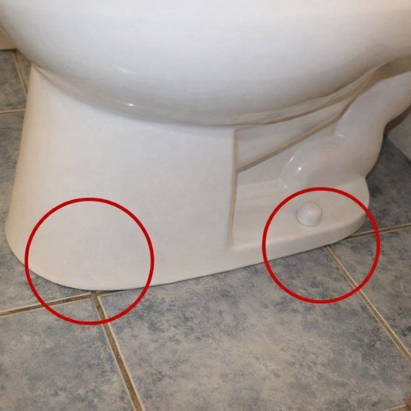 White toilet base on tiled floor, with two red circles highlighting its sides.