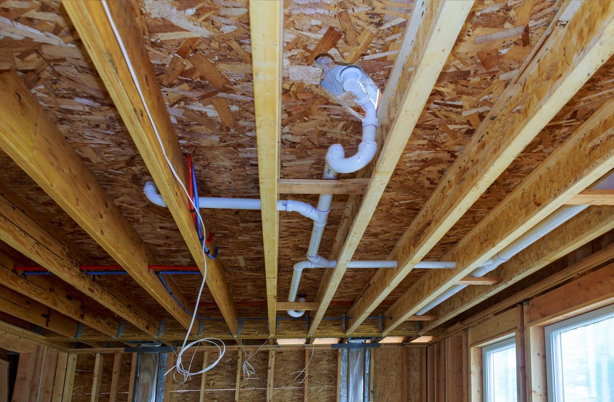 The ceiling of a house under construction with pipes coming out of it.