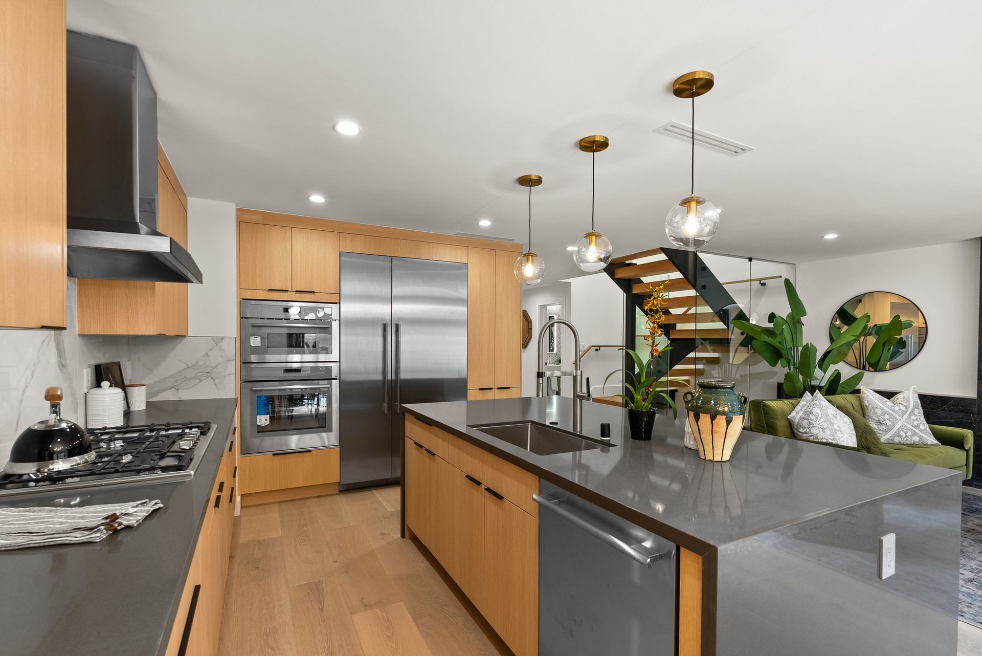 Modern kitchen with stainless steel appliances, gray island, wood cabinets, and a staircase in the background