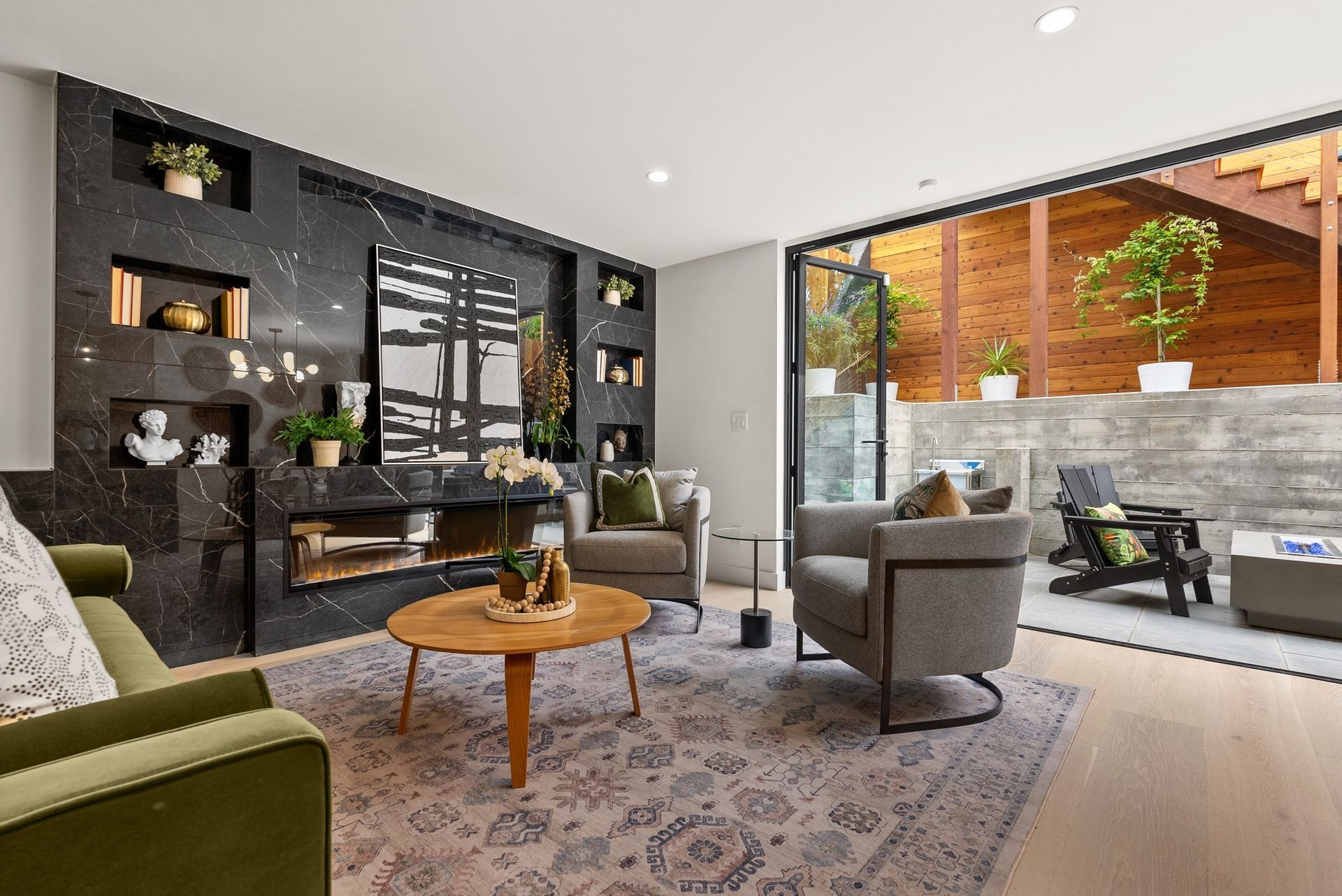 Modern living room with gray sofas, round wood coffee table, black accent wall, and large sliding glass doors