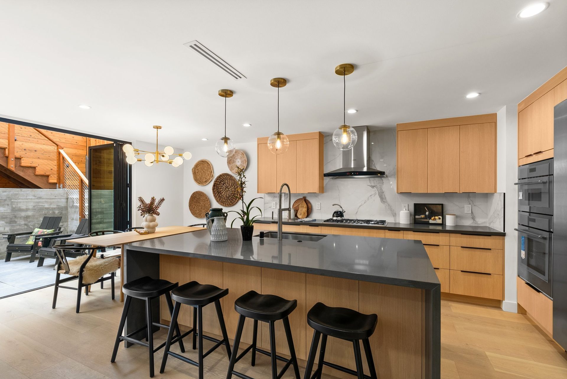 Modern kitchen with black island stools, wood cabinets, stainless appliances, and dining area beyond