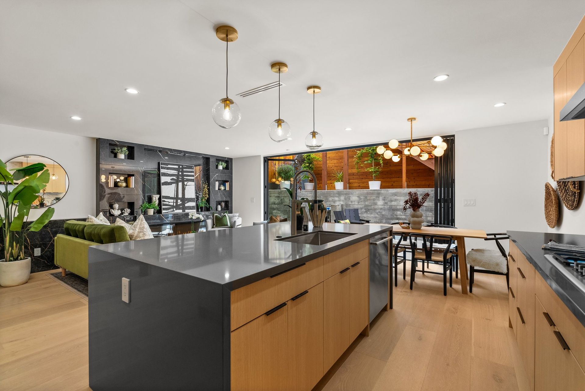 Modern open-plan kitchen with gray island, wood cabinets, brass pendant lights, and dining area