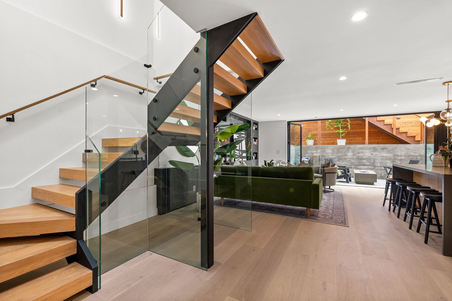 Modern open-plan interior with glass staircase, light wood floors, and dining area