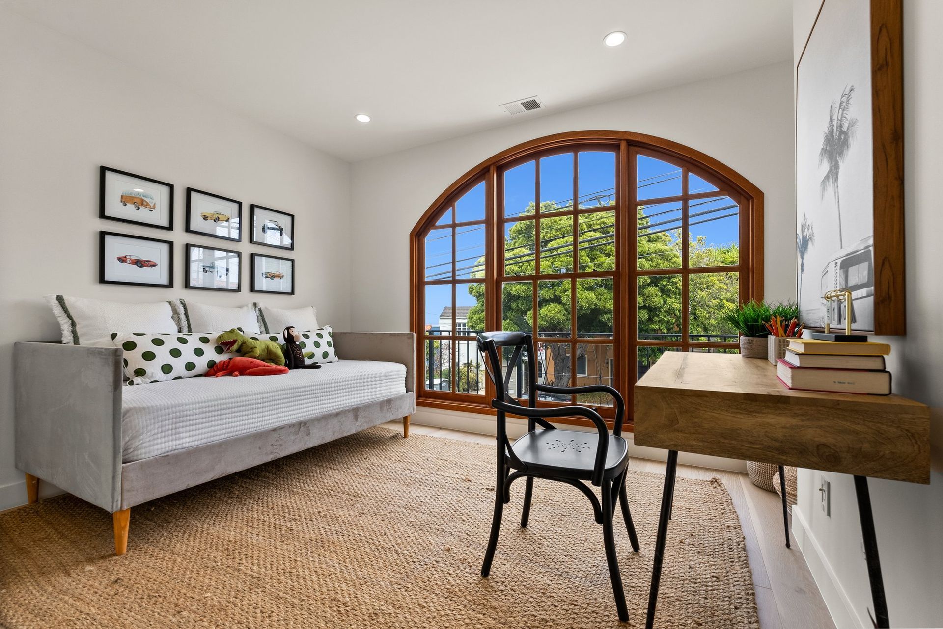 Bright bedroom with arched window, daybed, desk, and woven rug overlooking greenery