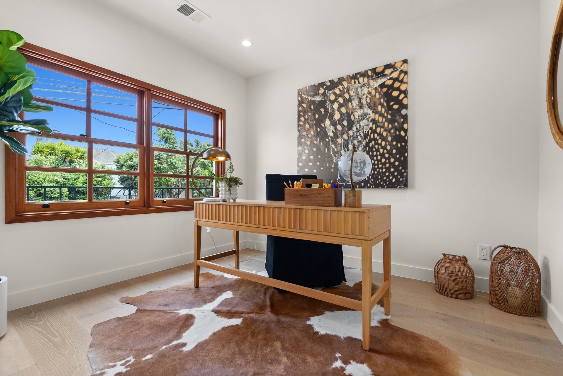 Bright home office with a wooden desk, cowhide rug, large window, and abstract wall art