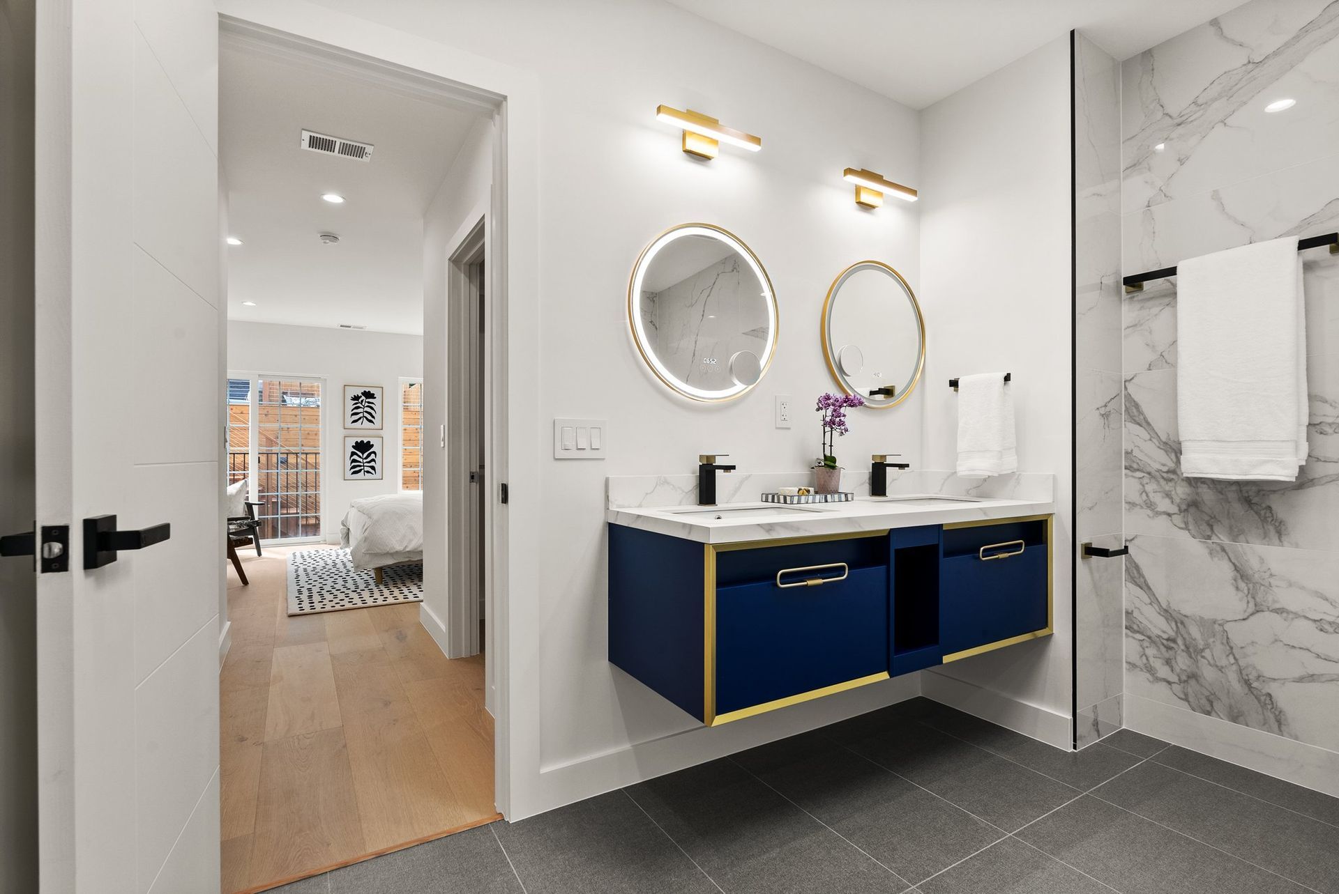 Modern bathroom with navy vanity, round mirrors, marble shower wall, and gray tile floor.
