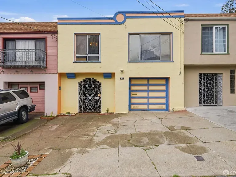 Row of narrow townhouses with garage doors and a cracked concrete driveway