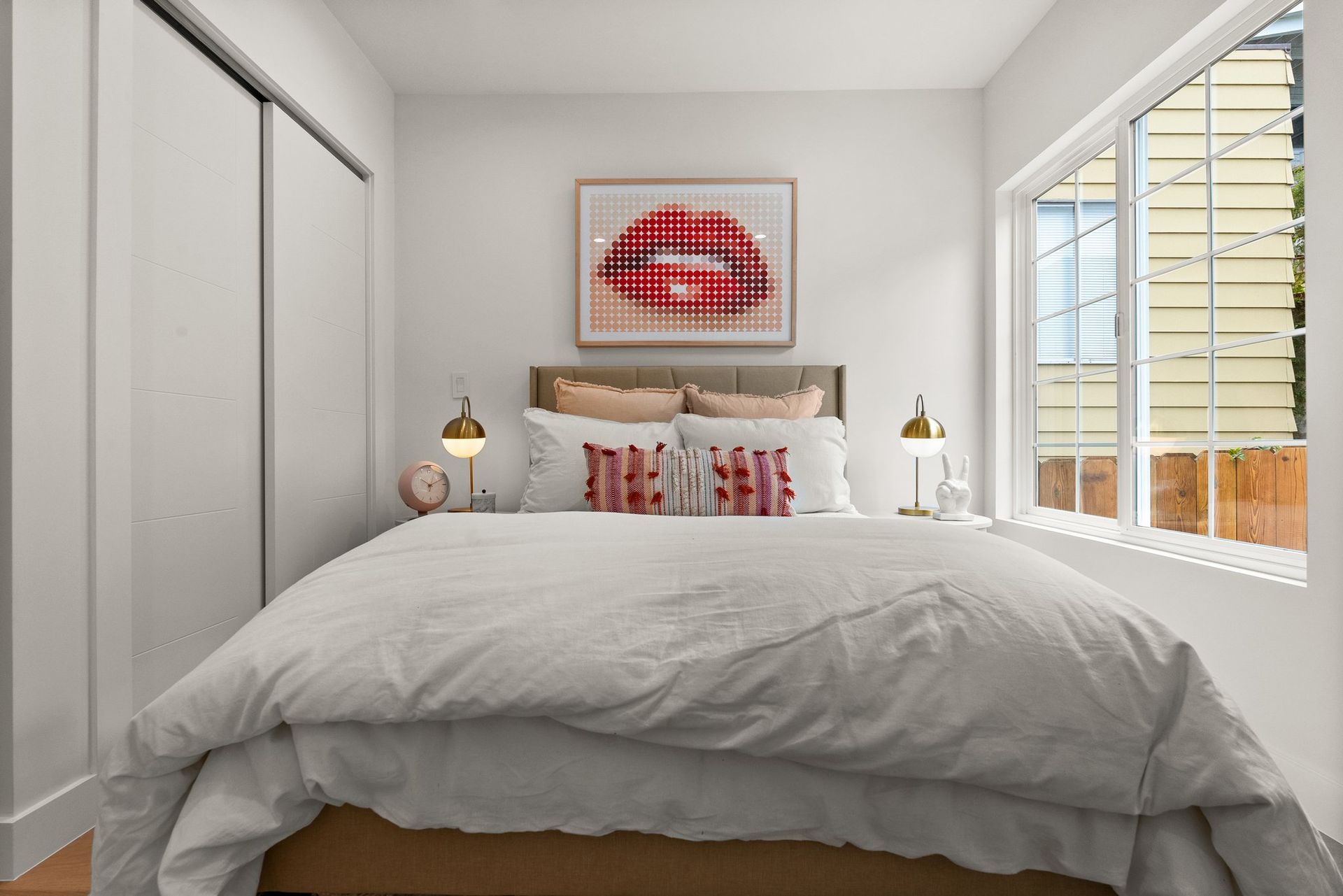 Bright bedroom with white bedding, red accents, and large windows overlooking an exterior wall