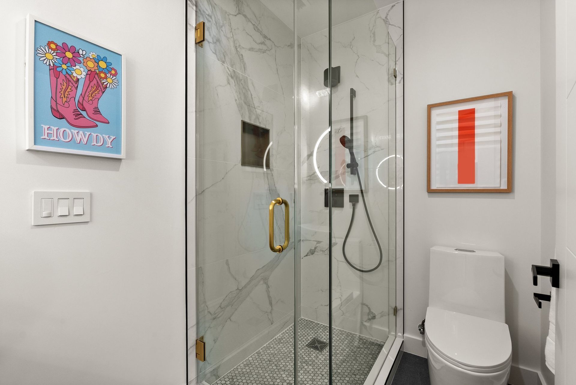 Modern bathroom with glass shower, white toilet, and colorful framed wall art.