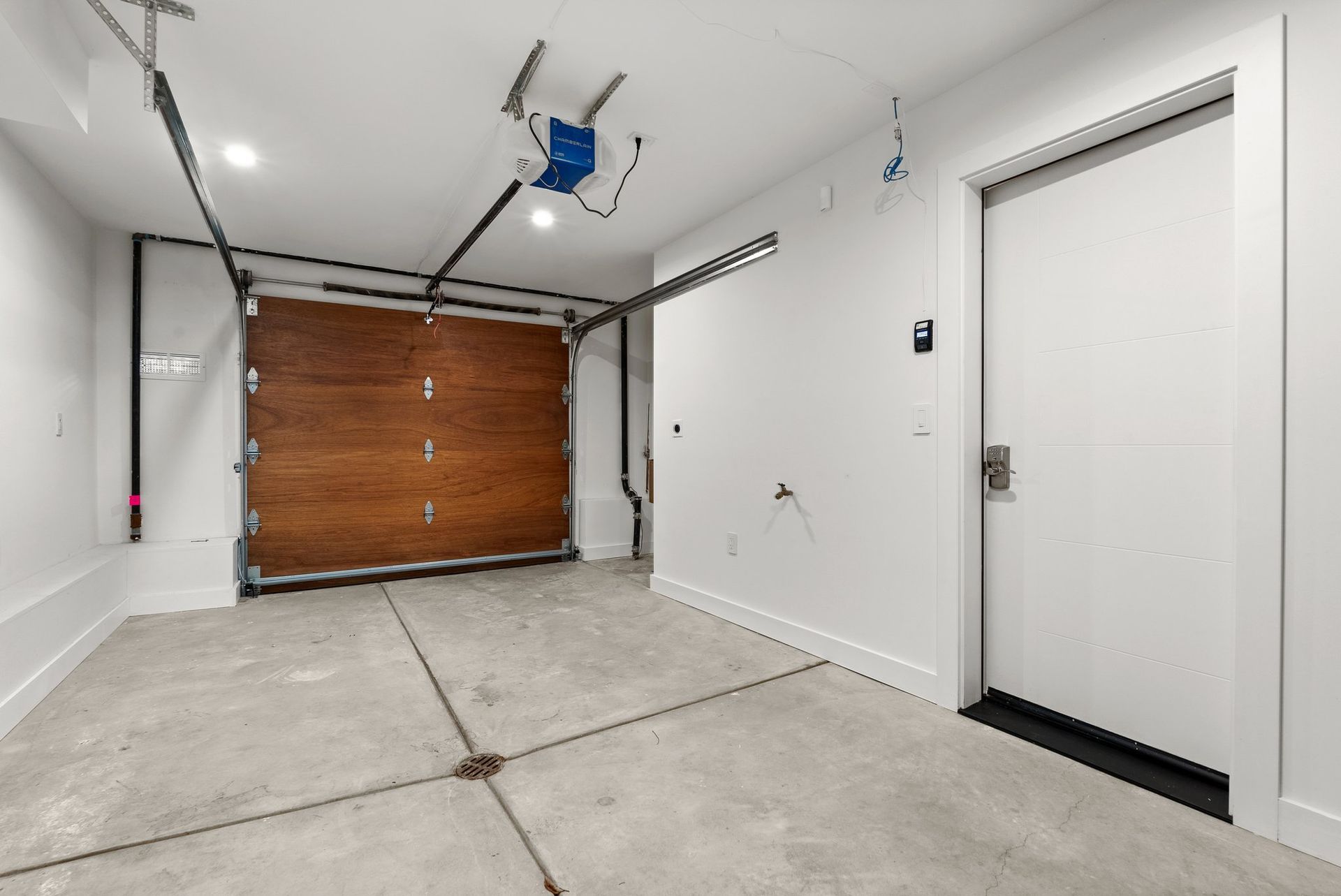 Empty residential garage with concrete floor, white walls, closed wooden garage door, and side entry door