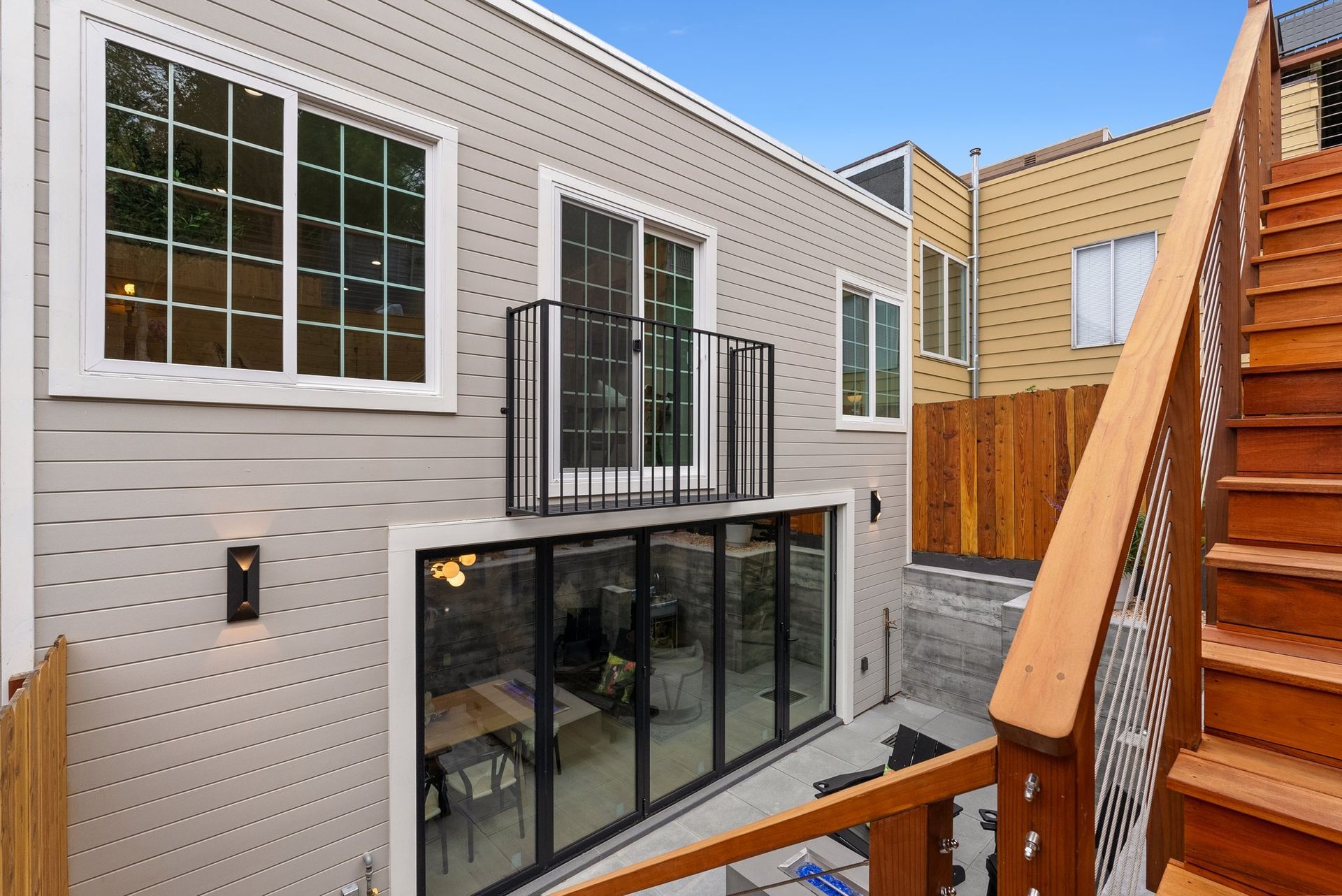 Outdoor patio between beige townhouses with black railings, large windows, and wooden stairs
