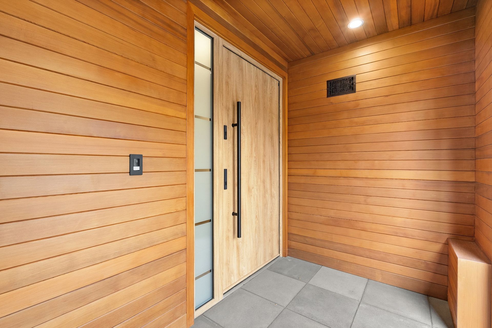 Wood-paneled front entry with a modern wooden door, tiled floor, and wall-mounted switch
