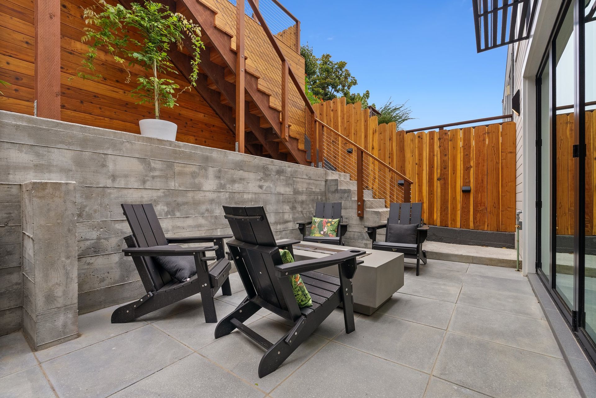 Modern patio with black chairs, concrete table, stone wall, wood fence, and glass sliding doors