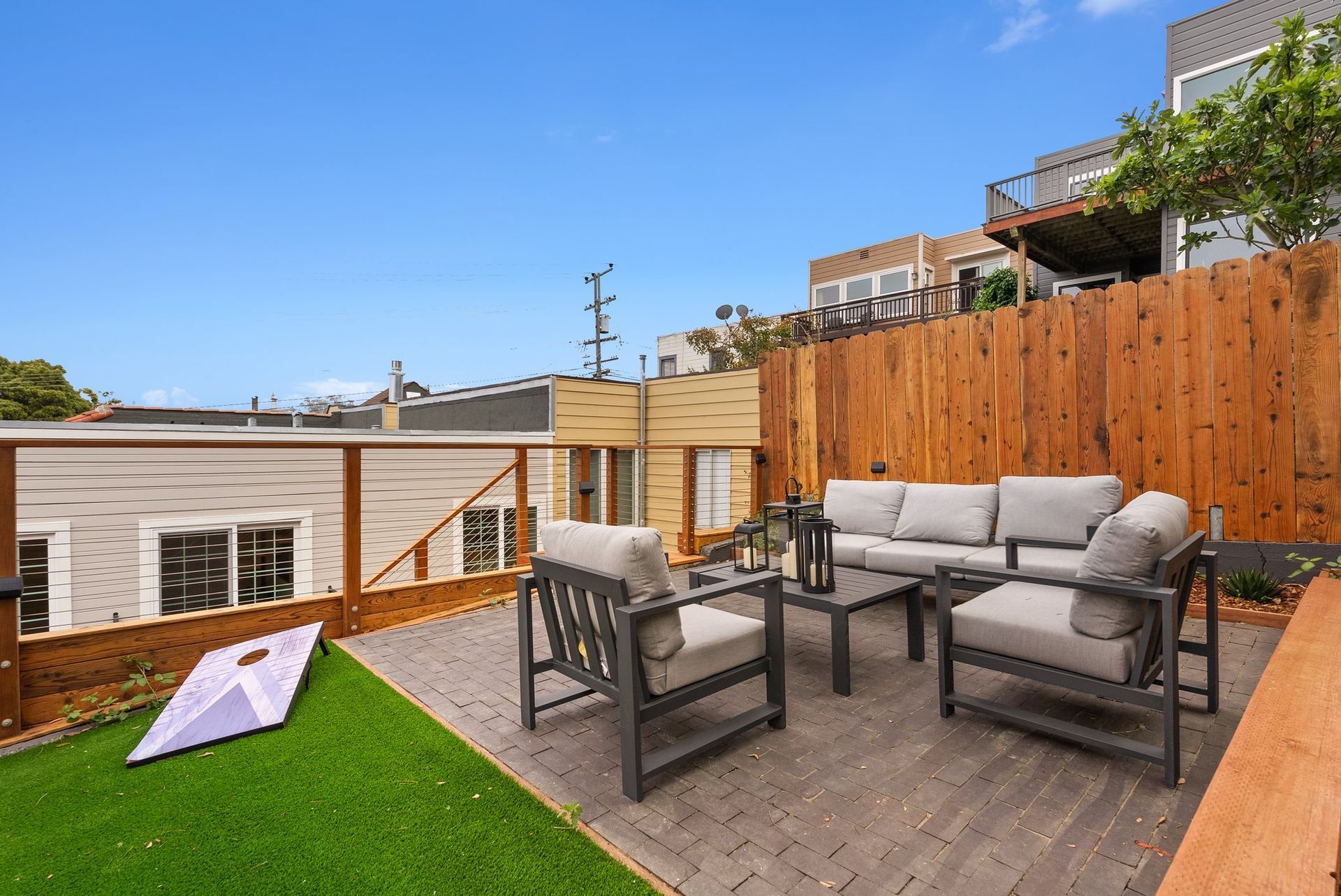 Rooftop patio with gray seating, wooden deck, green turf, and wooden fence under a blue sky