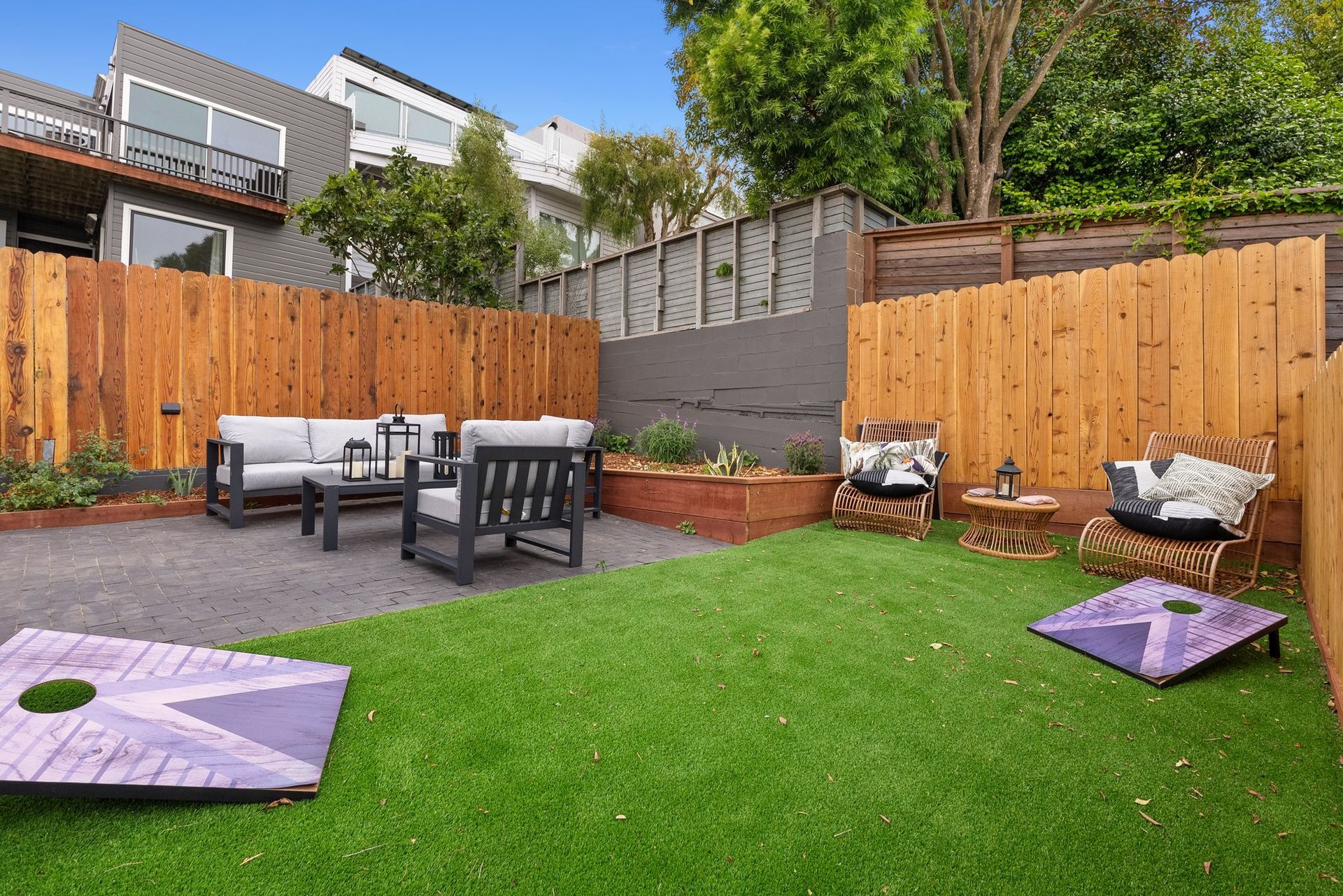Backyard patio with artificial grass, outdoor seating, wooden fences, and purple cushions
