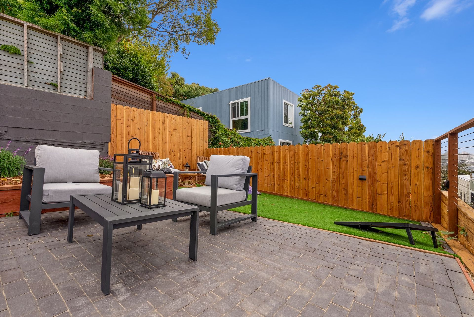 Patio with gray chairs, black table, and wood fence around a small grassy yard