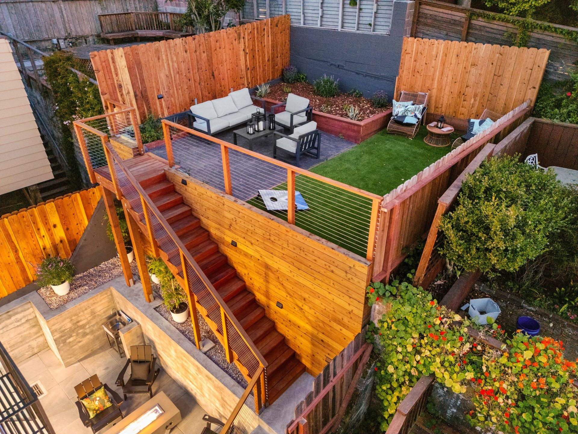 Aerial view of a small fenced backyard with patio furniture, wooden deck, string lights, and green turf