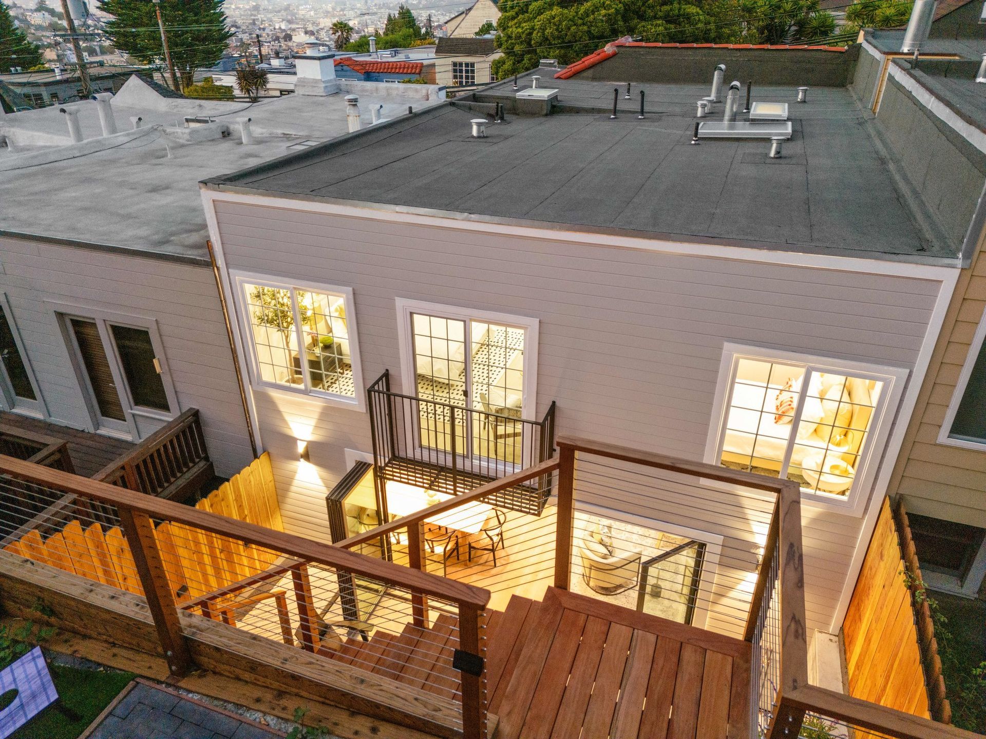 Rooftop deck with wooden stairs and railings beside a lit white building at dusk