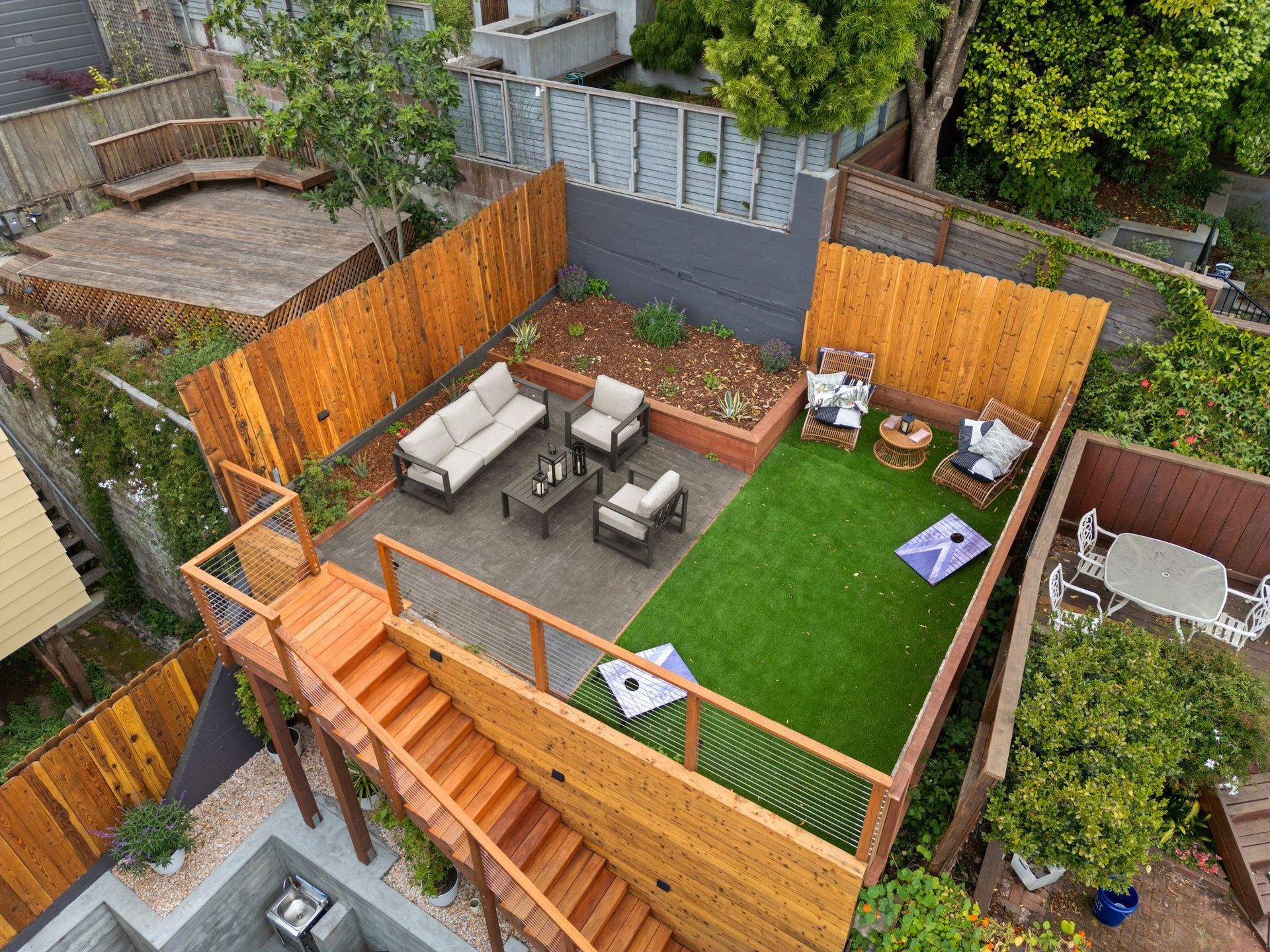 Small fenced backyard with artificial turf, patio furniture, wooden steps, and potted plants.