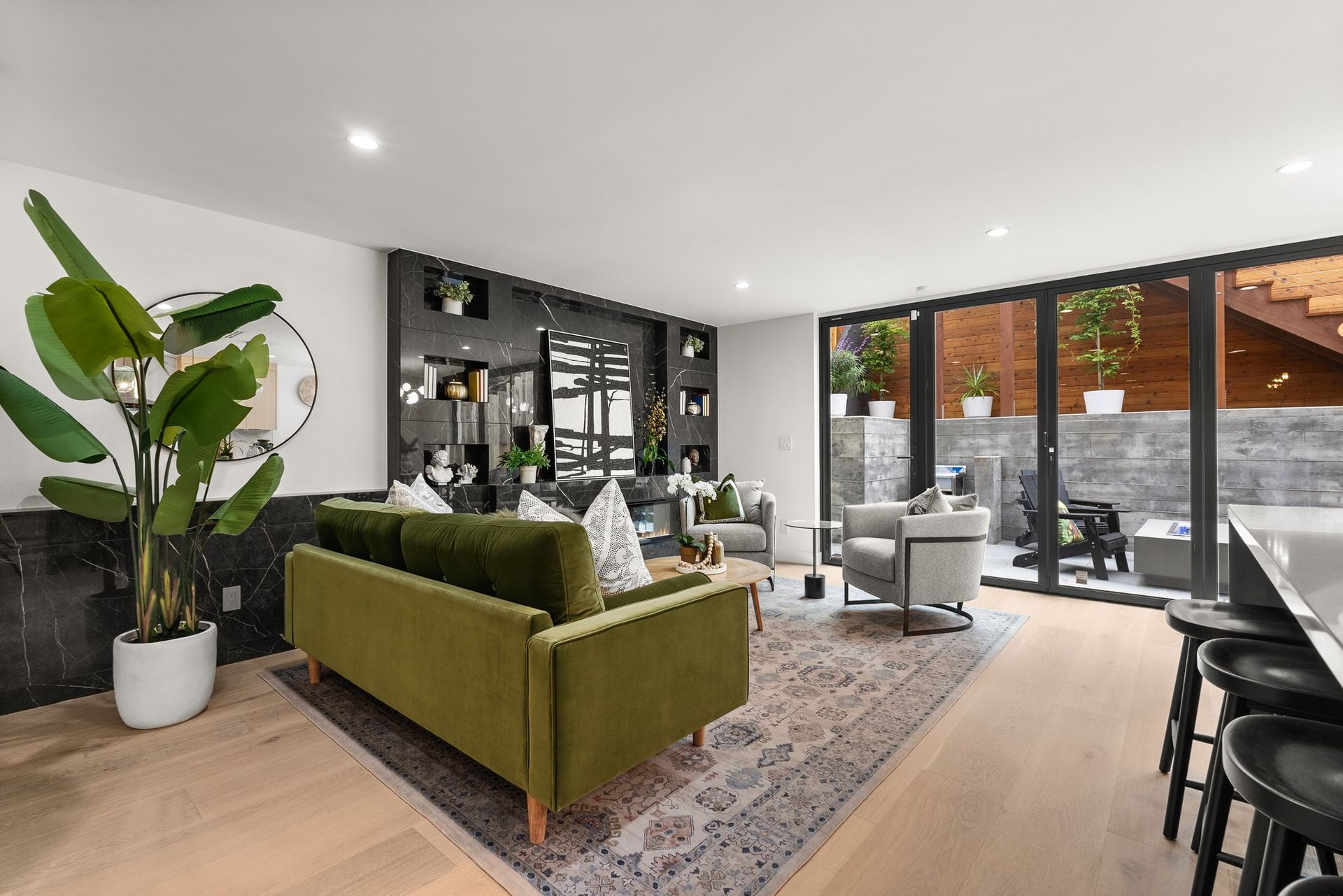 Modern living room with green sofa, black shelving, indoor plant, and large glass doors to a patio