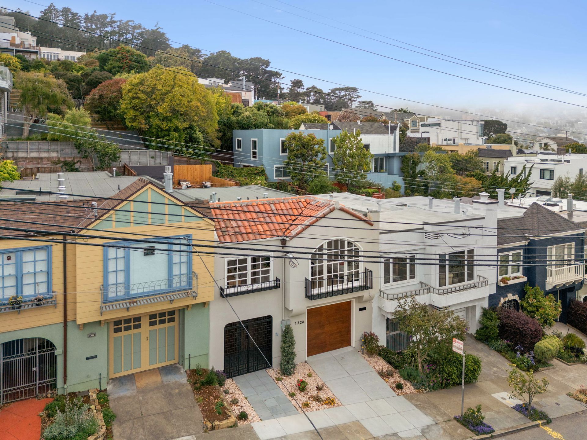 Row of colorful hillside townhouses with tiled roofs and balconies on a sunny residential street