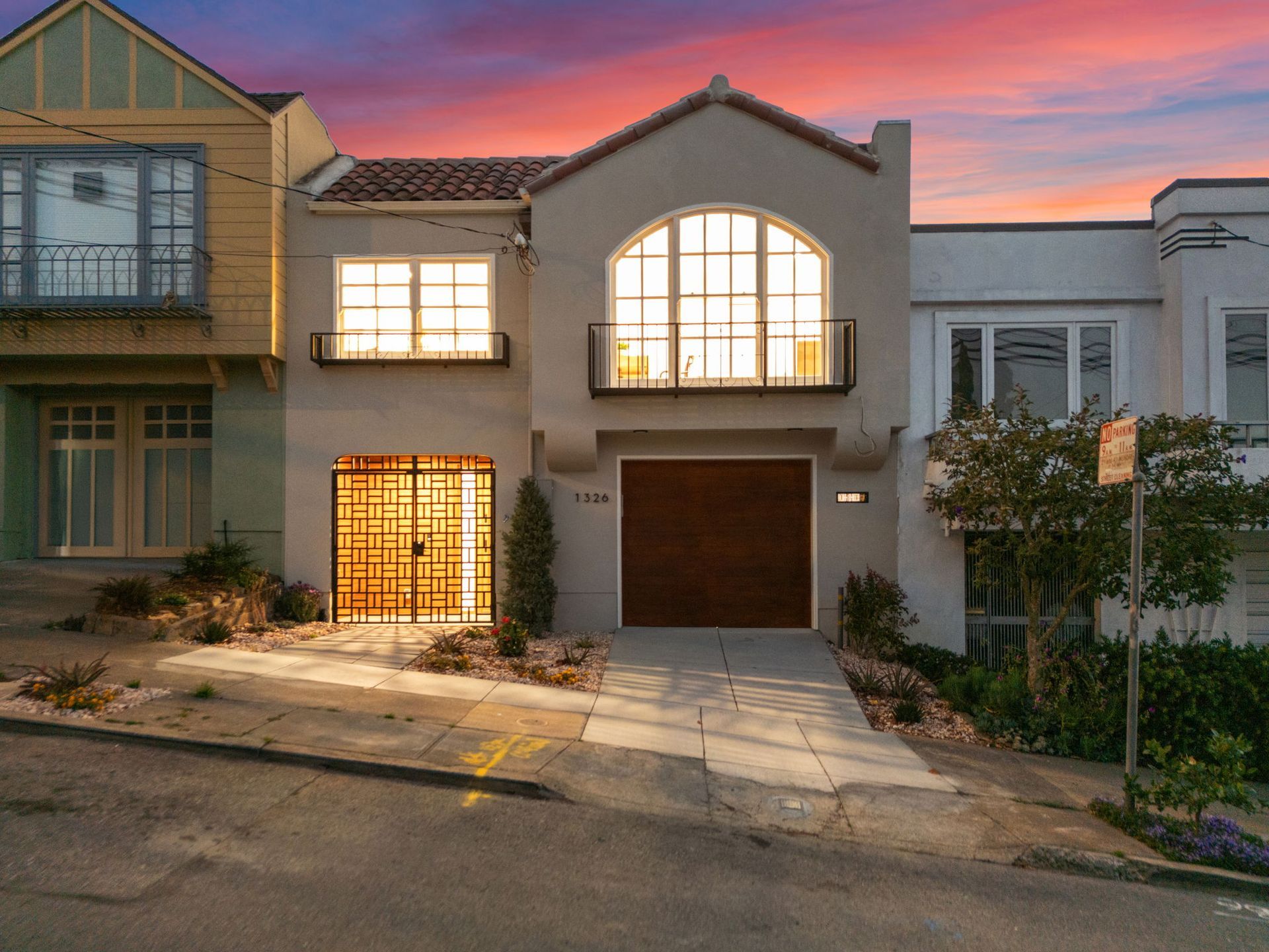 Modern townhouse with lit windows and garage at dusk, under a pink-orange sky.