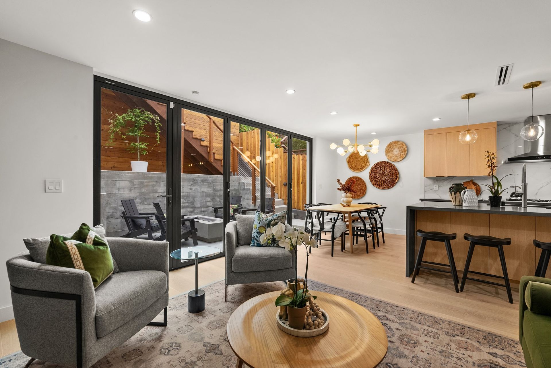 Bright open-concept living room with gray chairs, dining table, kitchen island, and sliding doors to a patio