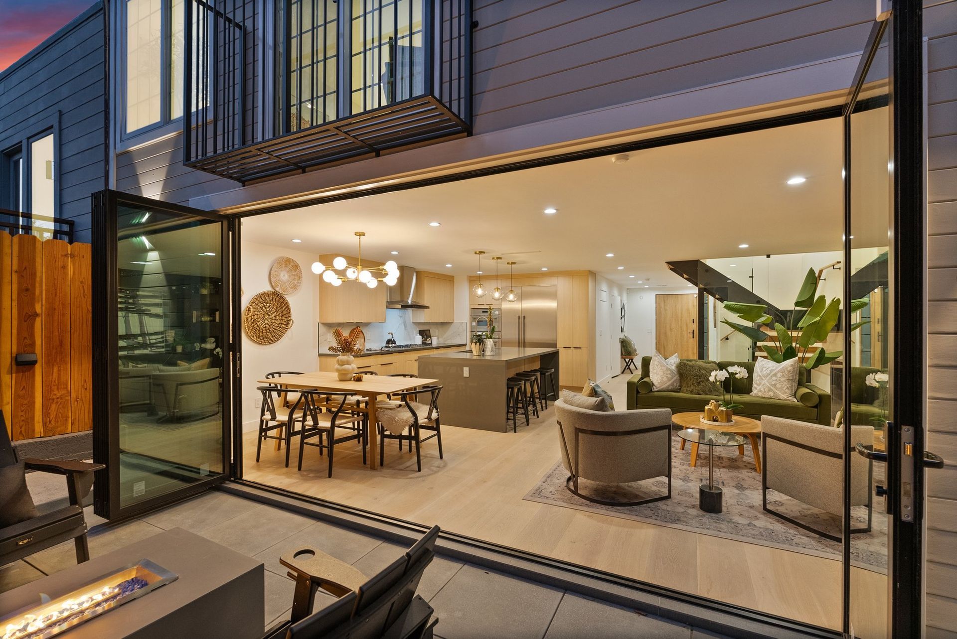 Modern open-plan living room and kitchen with large glass doors, warm lighting, and patio seating