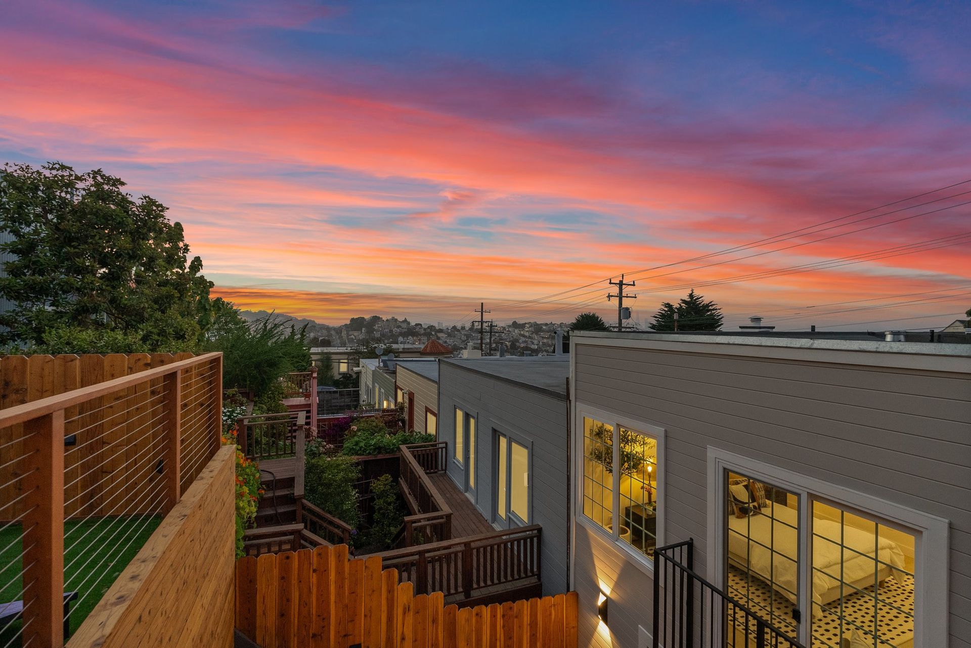 Backyard deck and modern homes at sunset under a pink-orange sky