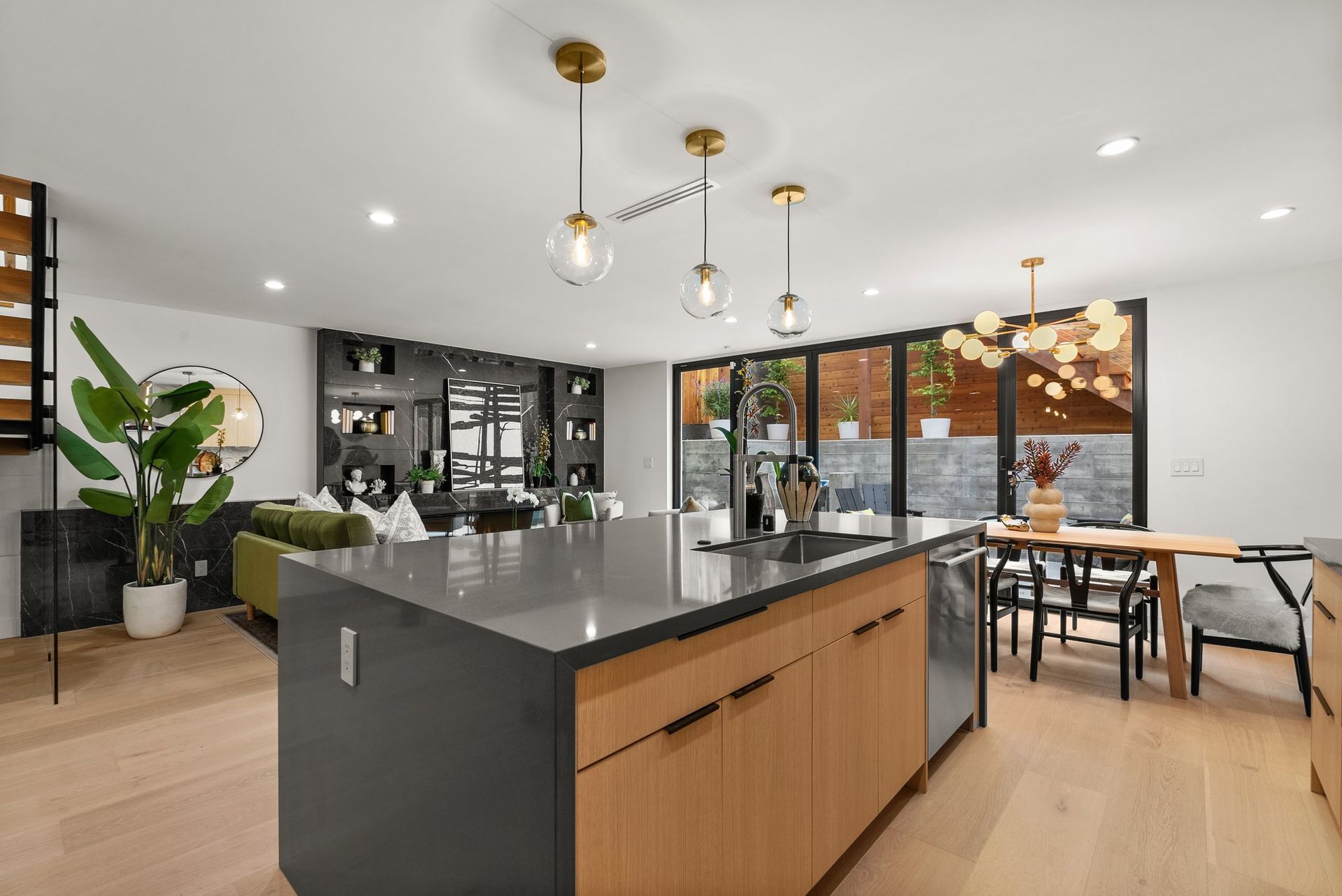 Modern open-plan kitchen with island, wood cabinetry, black countertops, and dining area by large windows