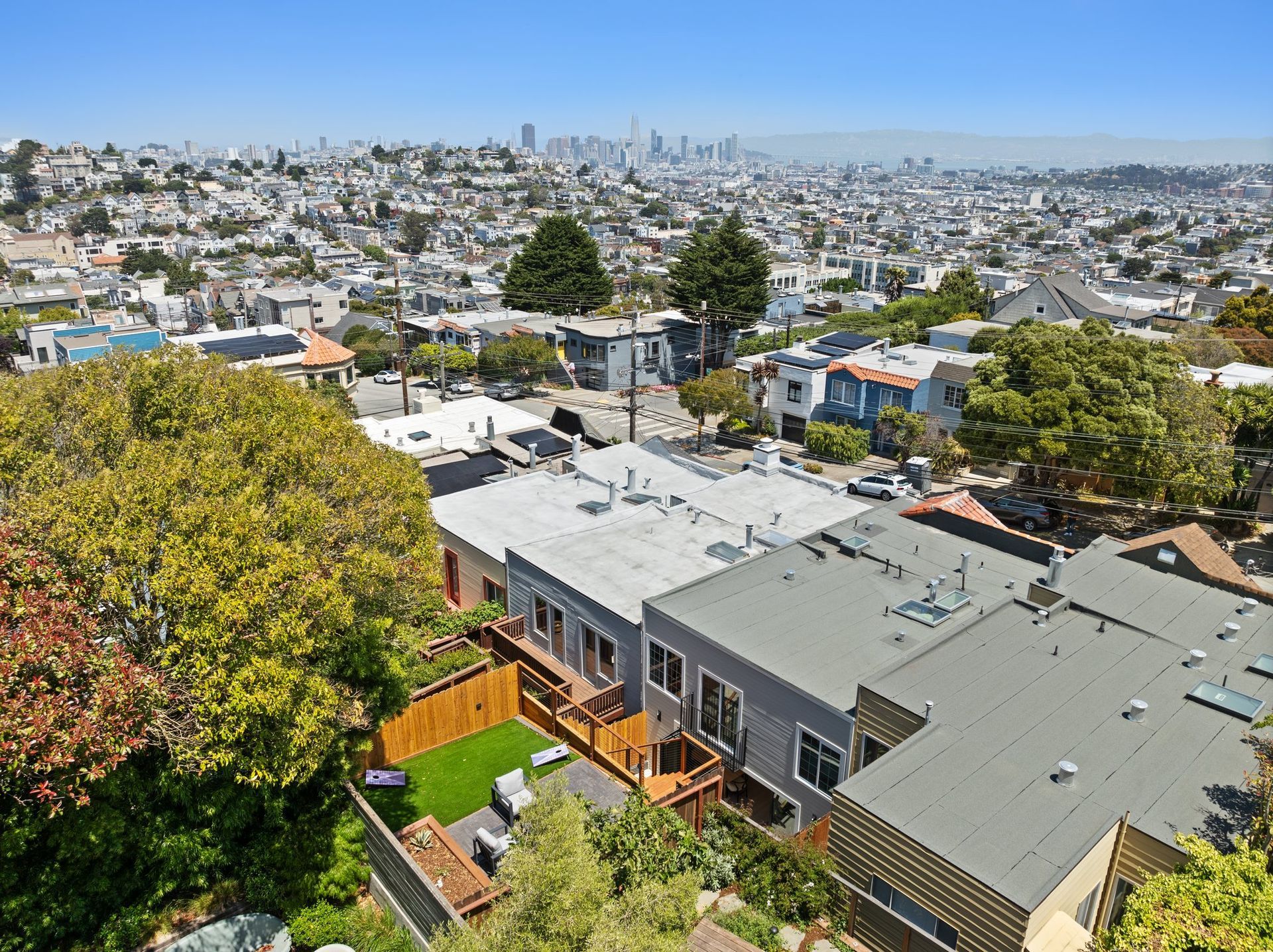 Sunny hillside neighborhood with rooftops, trees, and a city skyline in the distance