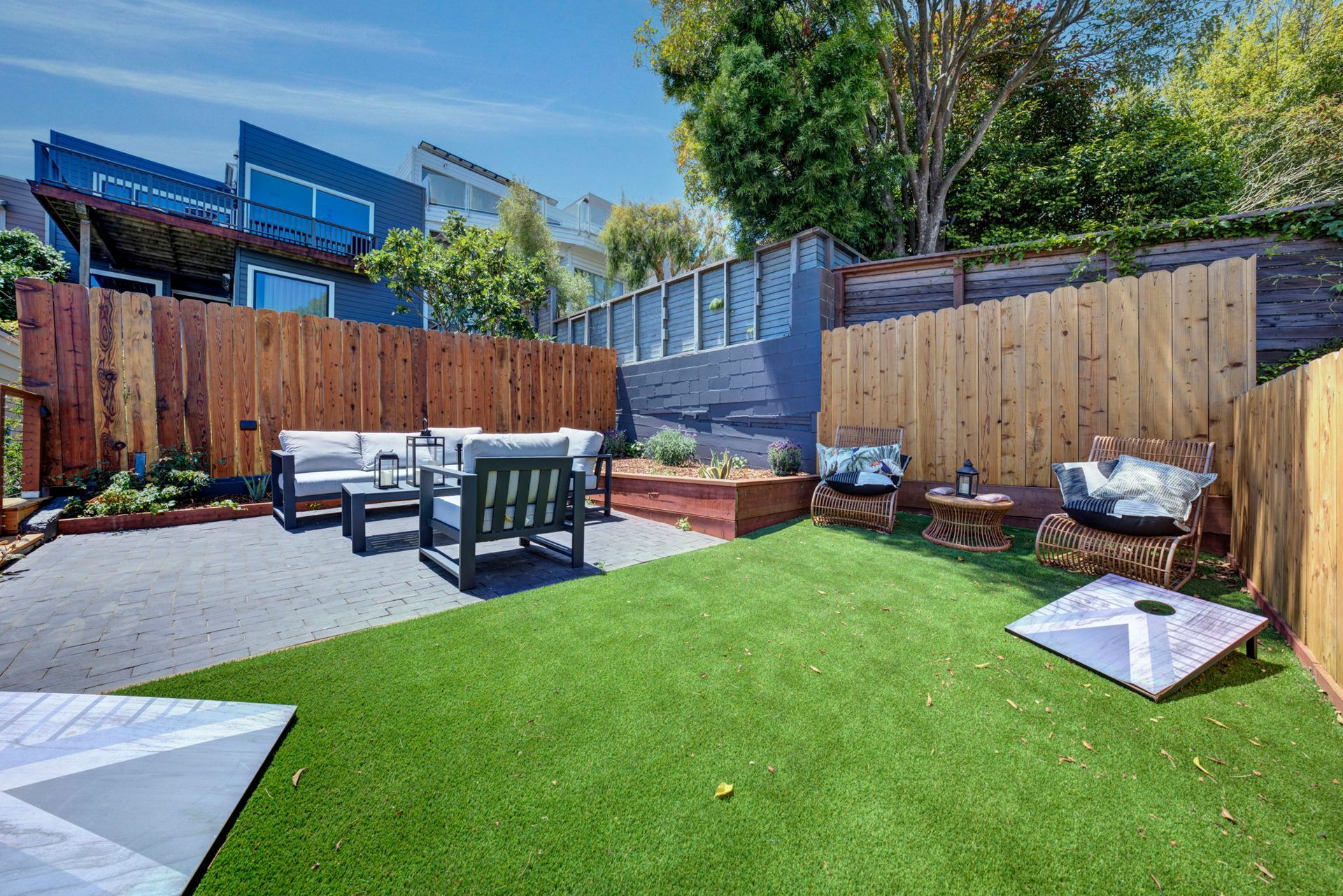 Backyard patio with green lawn, outdoor seating, wooden fences, and modern buildings beyond