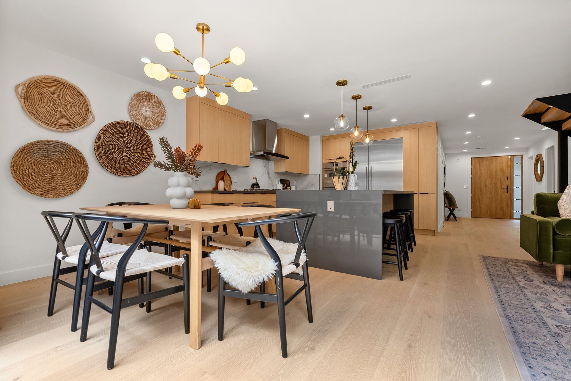Modern open-concept dining and kitchen area with wood accents, metal chairs, and woven wall decor