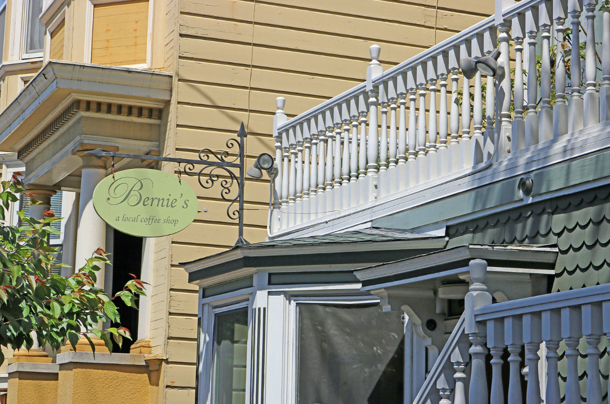 Storefront with green hanging sign and blue balcony railing on a tan building