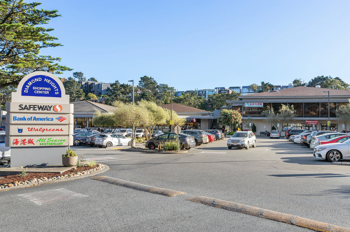 Motel entrance with parking lot, cars, and roadside sign under a clear blue sky