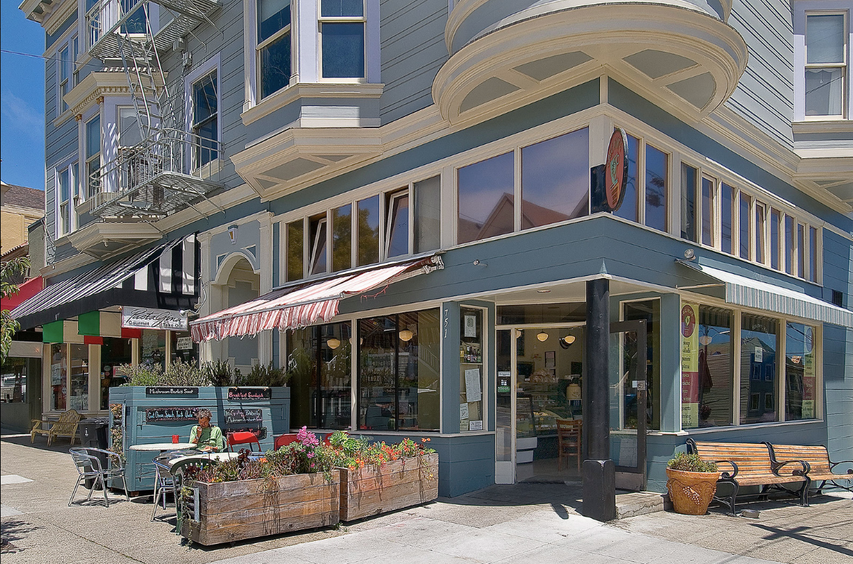 Corner café with striped awnings, flower planters, and outdoor seating on a sunny street corner