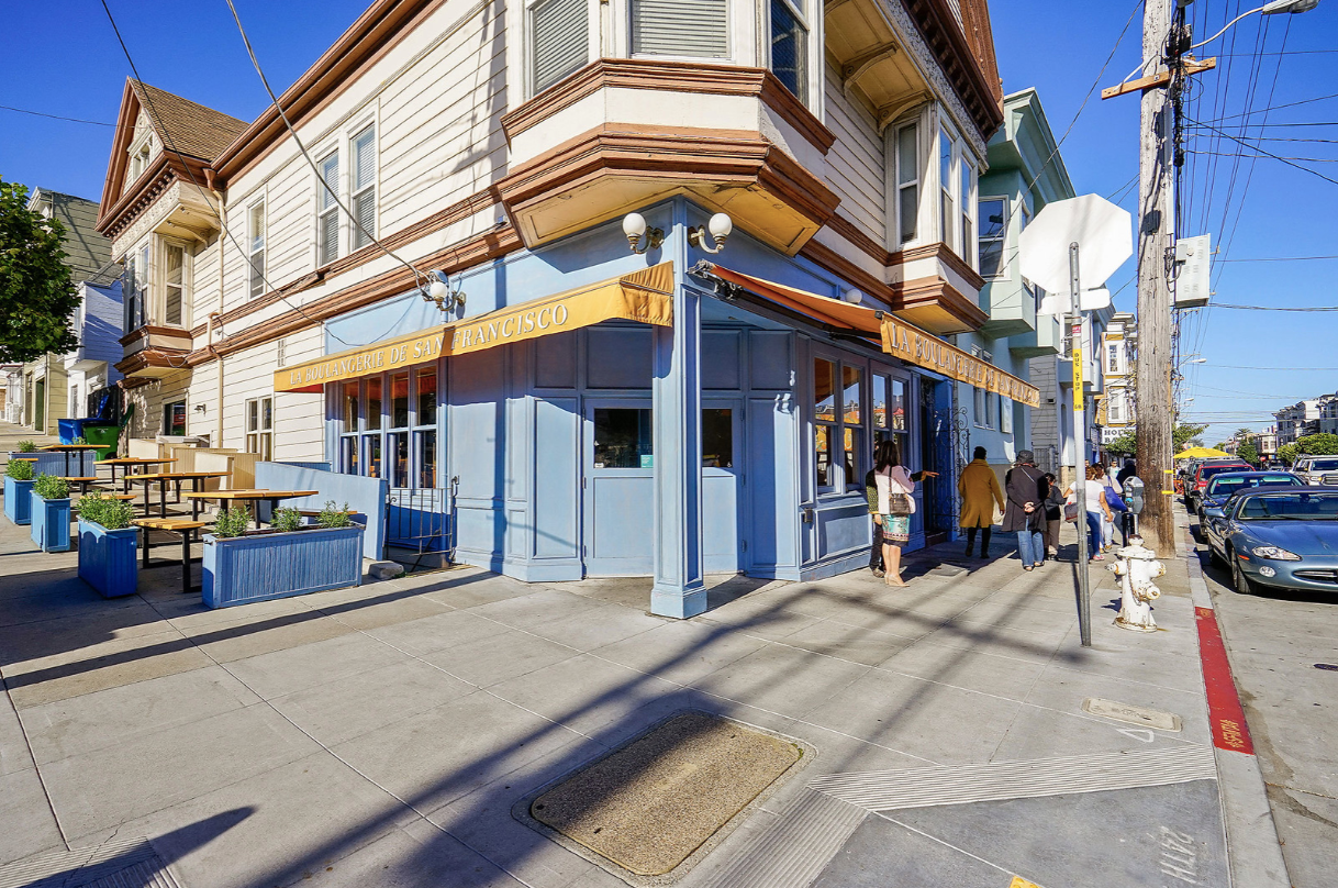 Sunny street corner with a blue-and-white building and pedestrians on the sidewalk